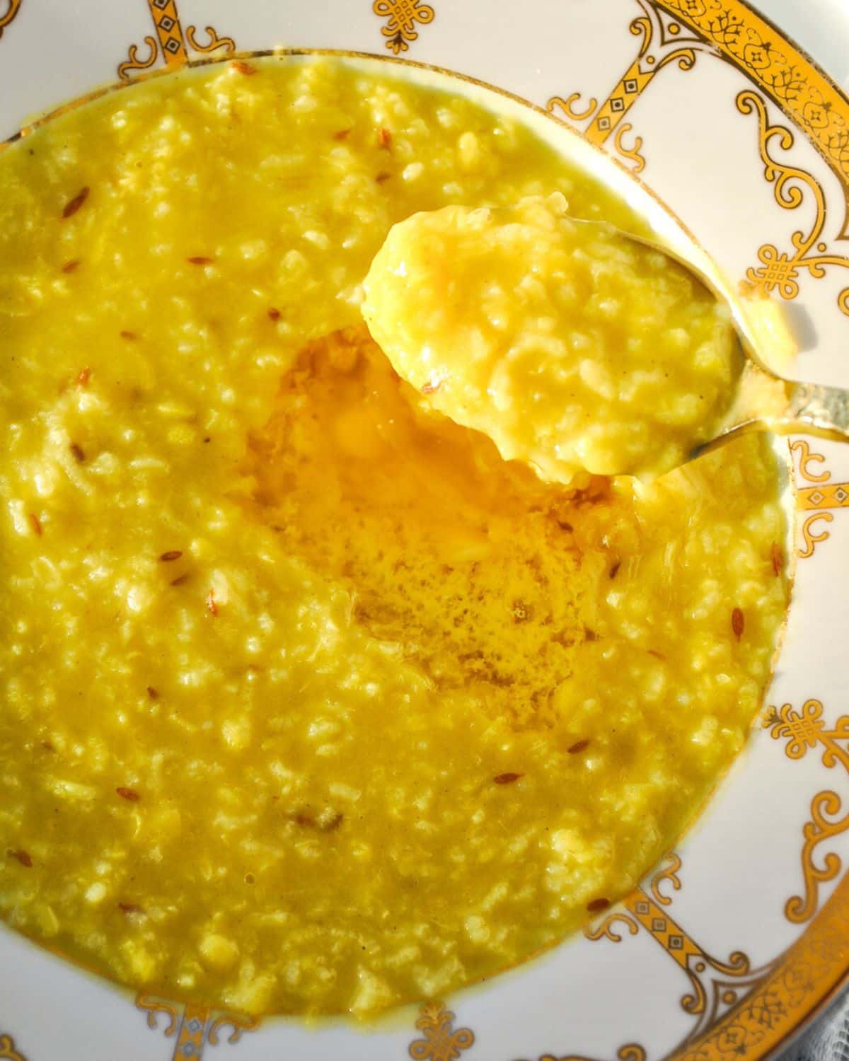 A bowl of khichdi with melted butter with a spoonful above the bowl.
