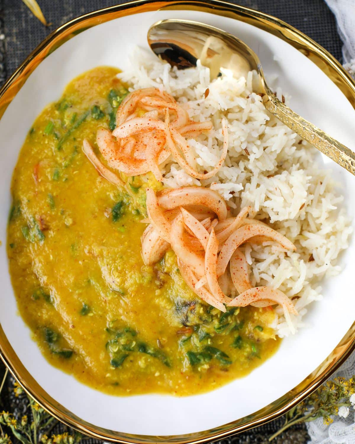 Masoor Dal with jeera rice and laccha onions in a white bowl with gold trim and a gold spoon.