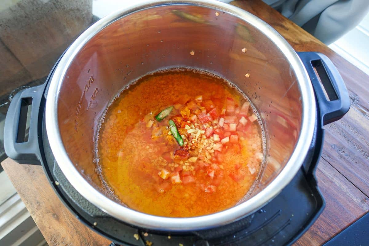 Uncooked Masoor Dal in the Instant Pot with tomatoes, green chiles, garlic, turmeric powder, and salt.