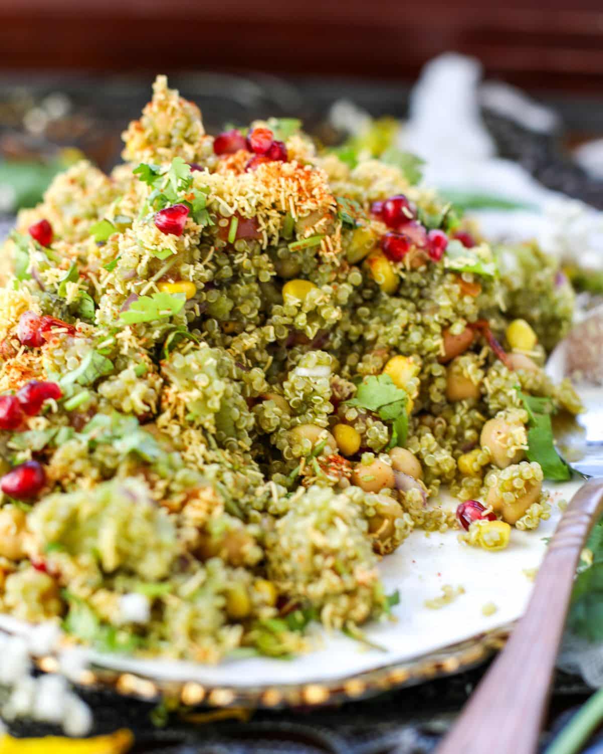 Quinoa Bhel Salad on a serving plate with a large spoon garnished with sev, cilantro, and pomegranate.
