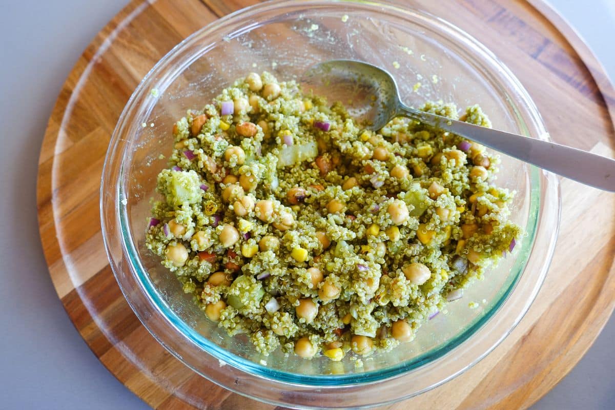 A clear bowl with mixed Quinoa Bhel Salad and a spoon.