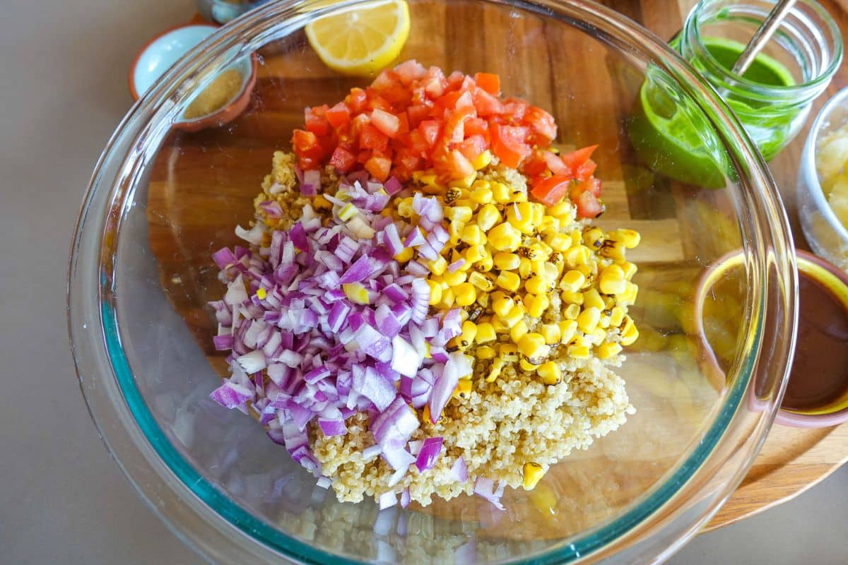 A clear bowl with quinoa, tomatoes, red onions, and corn for Quinoa Bhel Salad.