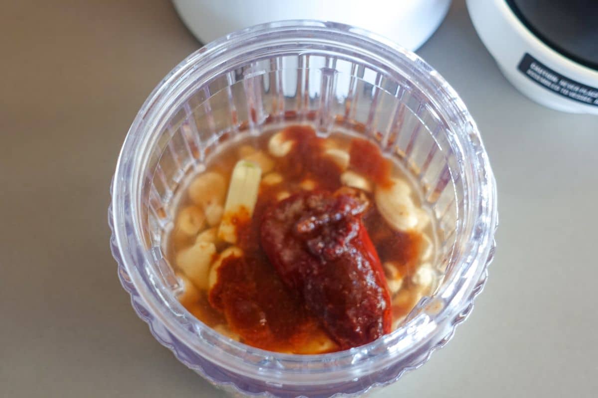 A blender containing cashews, chipotle peppers, garlic, and water to be blended.