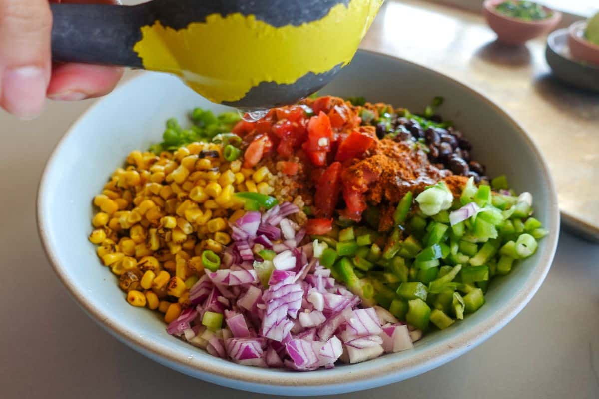 A bowl with chopped red onion, green pepper, tomato, black beans, corn, scallion, and spices; lemon juice is being squeezed over the ingredients.
