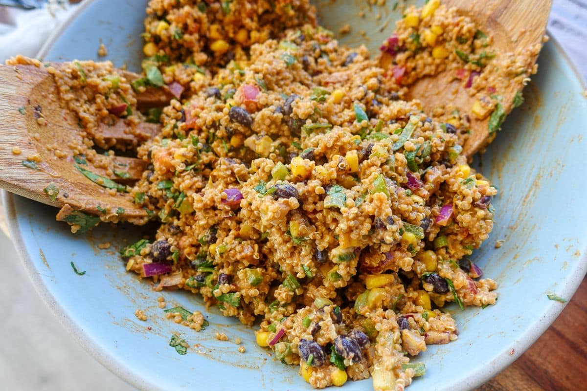 A bowl of mixed quinoa salad with black beans, corn, chopped vegetables, and herbs.