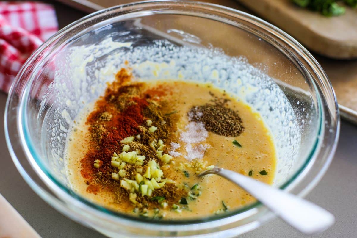 A glass bowl with besan batter along with ginger, spices, and salt.