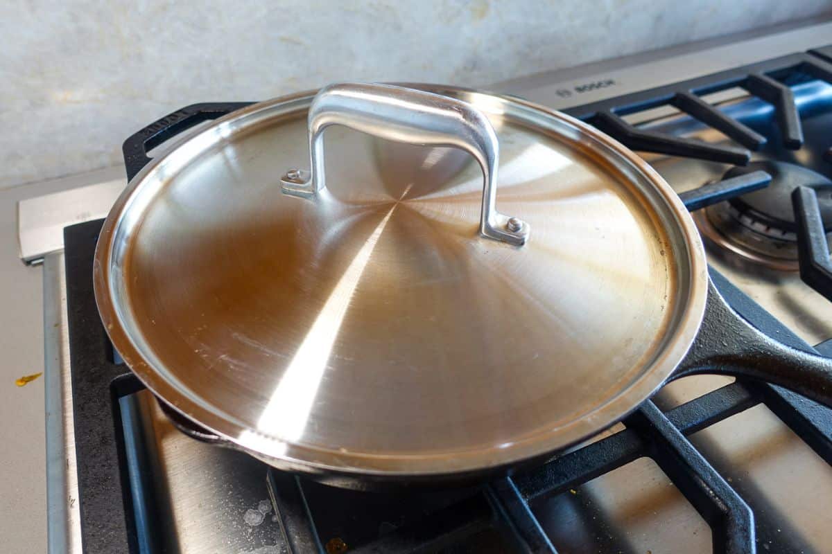 A stainless steel pan with a lid sits on a gas stove burner.