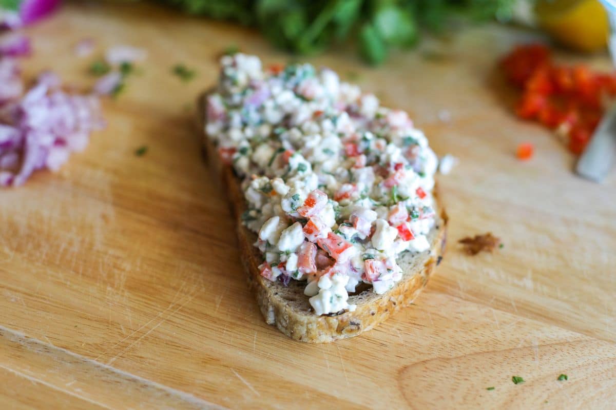 A slice of sourdough bread topped with a mixture of cottage cheese and herbs on a wooden cutting board.