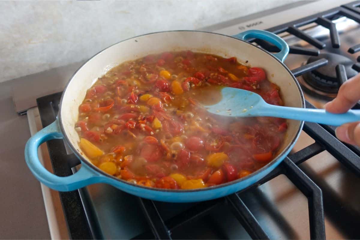 Gently press on chopped tomatoes in a blue enameled pan on a gas stove, cooking a sauce.
