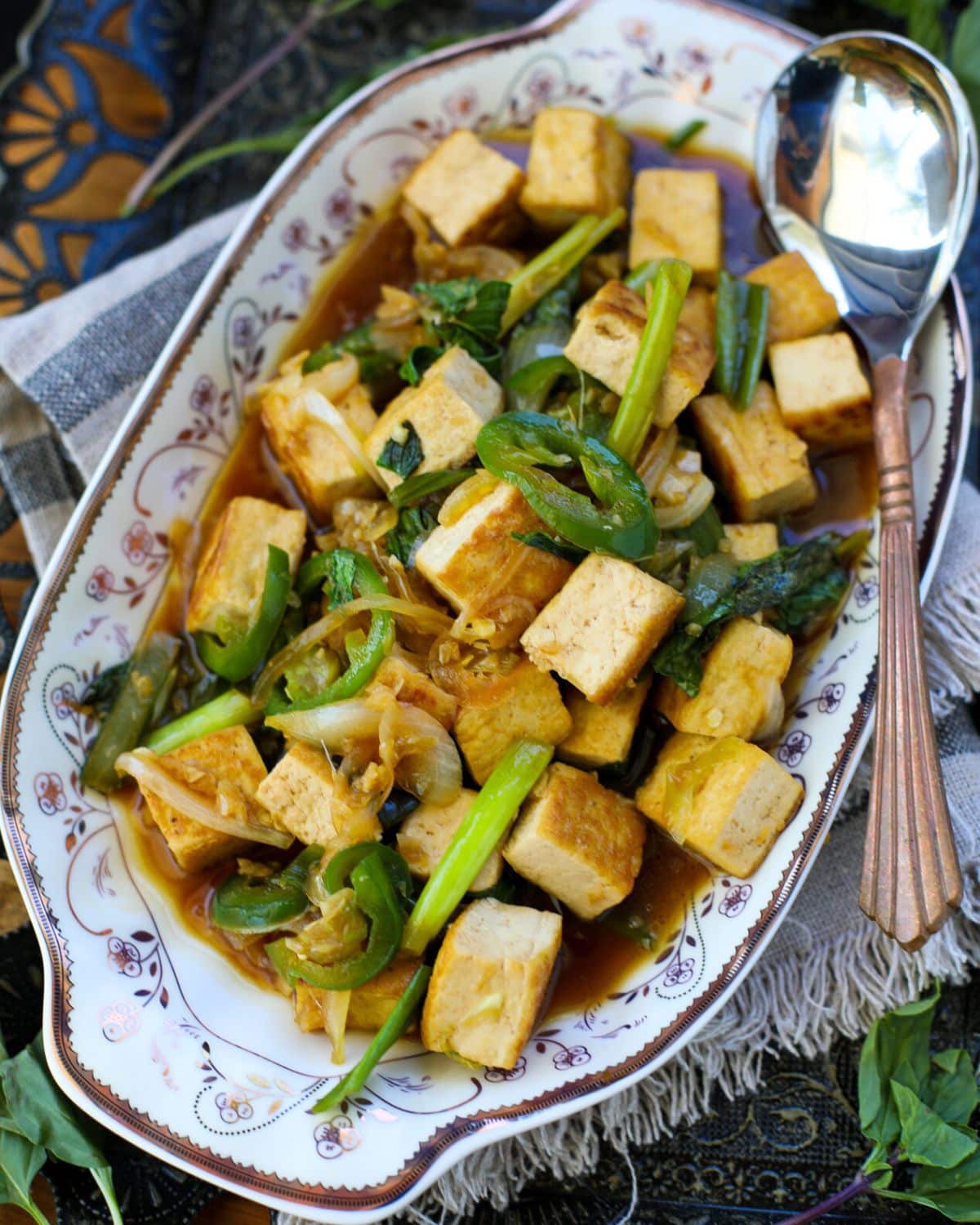Thai Basil Tofu with Garlic and Jalapeno filled with stir-fried tofu, scallions, onions, and sauce, with a serving spoon on the side.