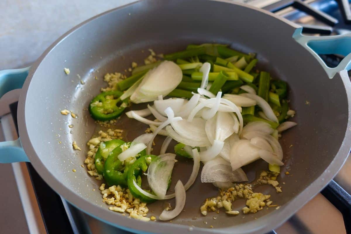 Add sliced onions and scallions in a ceramic frying pan on a stovetop.