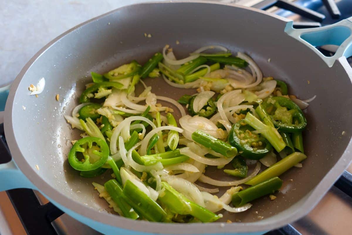 Sauteed veggies in a light blue skillet on a stove.
