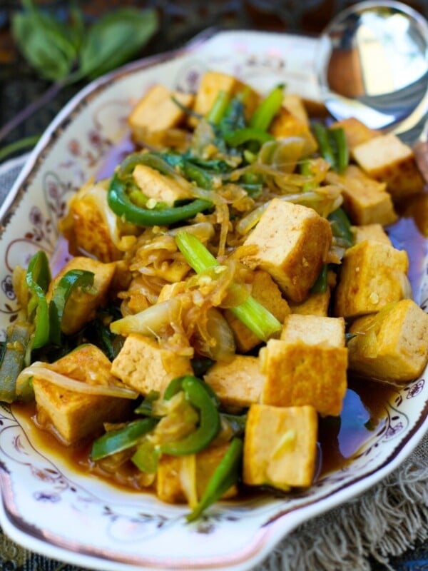 Thai Basil Tofu with Garlic and Jalapeno filled with stir-fried tofu, scallions, onions, and sauce, with a serving spoon on the side.