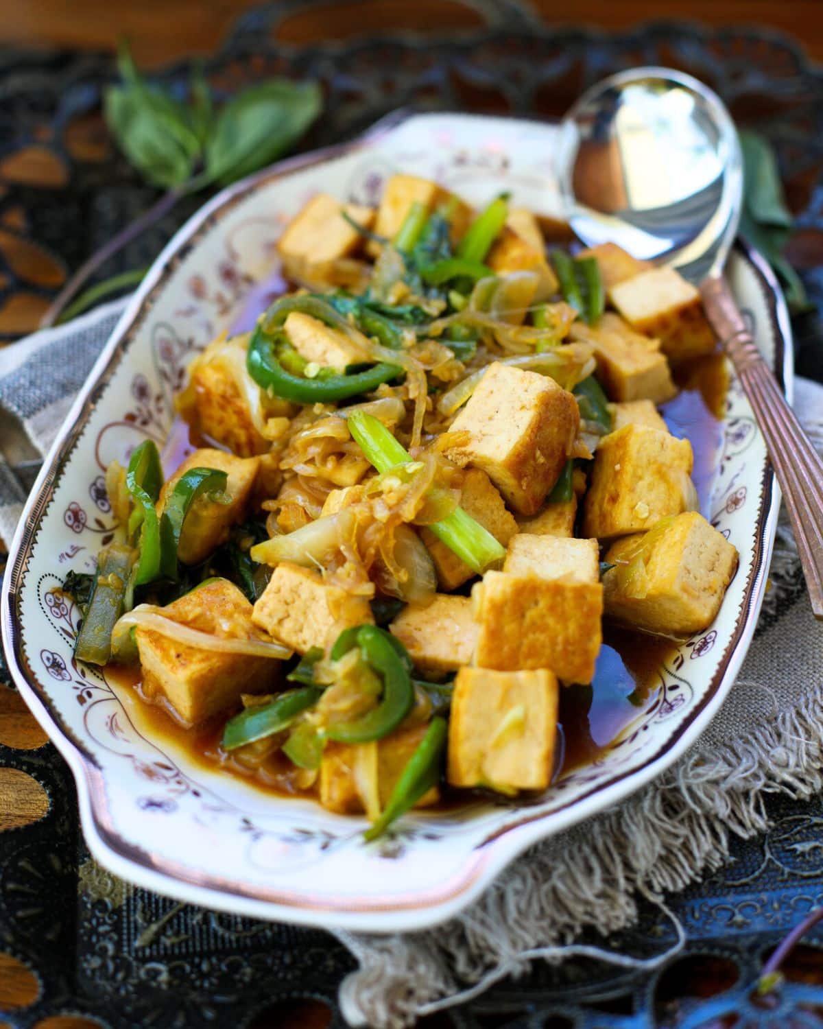 Thai Basil Tofu with Garlic and Jalapeno filled with stir-fried tofu, scallions, onions, and sauce, with a serving spoon on the side.