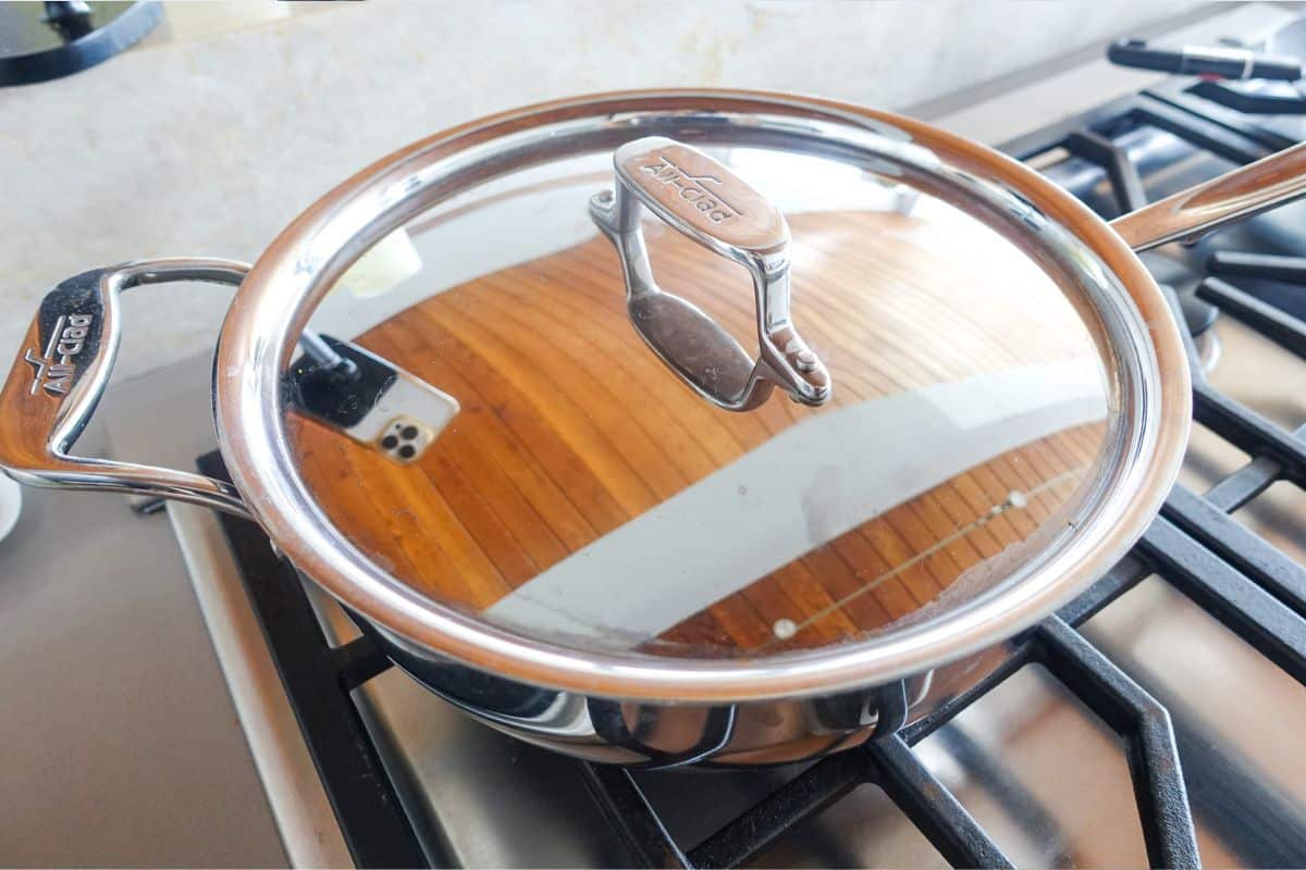A stainless steel saucepan with a lid sits on a gas stove burner.