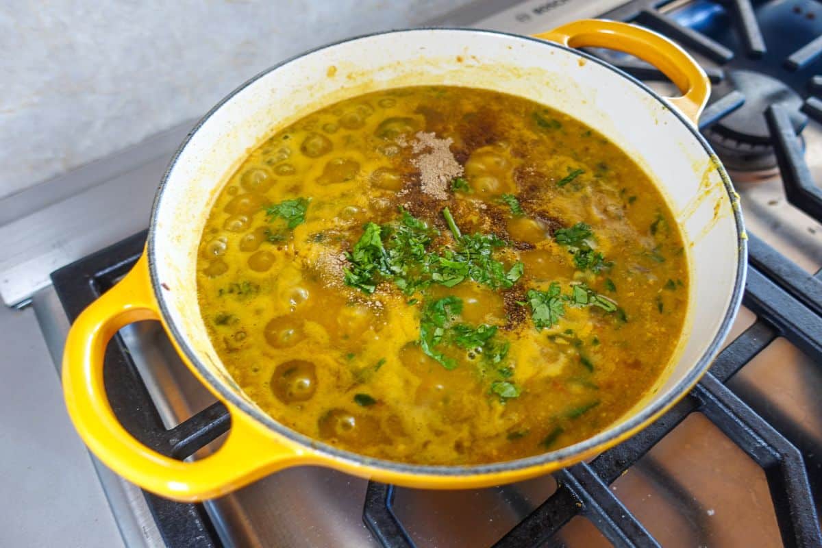 A yellow pot on a stove contains simmering dal, garnished with chopped cilantro and spices on top.