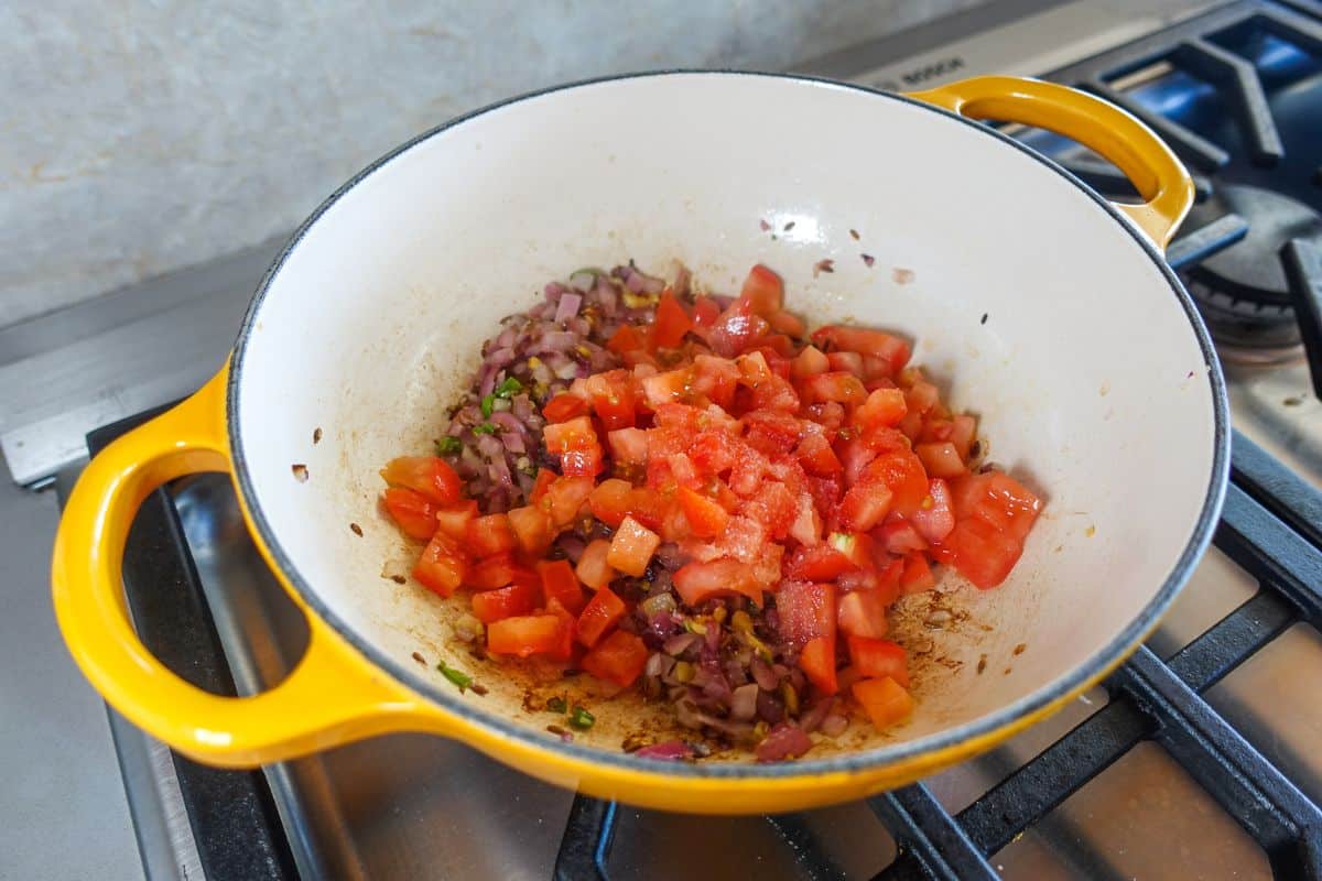 Chopped tomatoes with salt are added in a yellow pot on a gas stove.