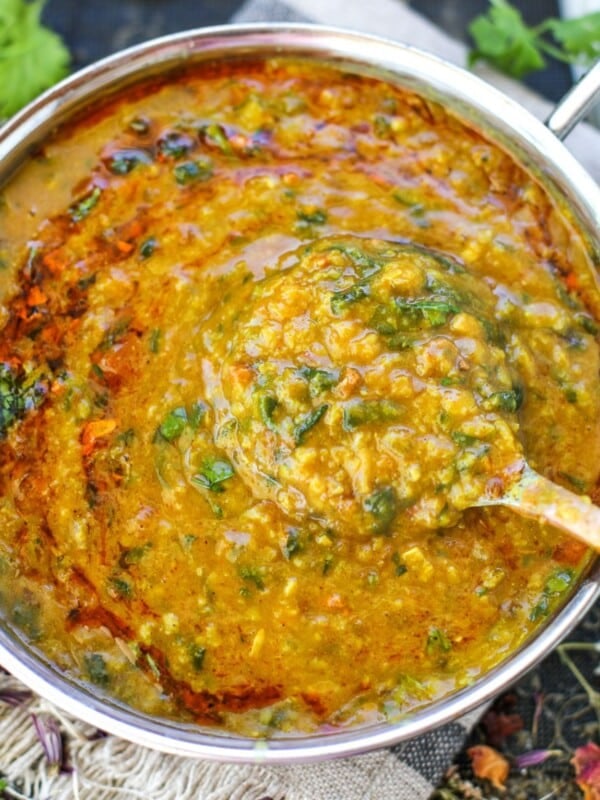 A pot of cooked spinach dal fry with cilantro and garlic tadka, and a ladle lifting a portion from the center.