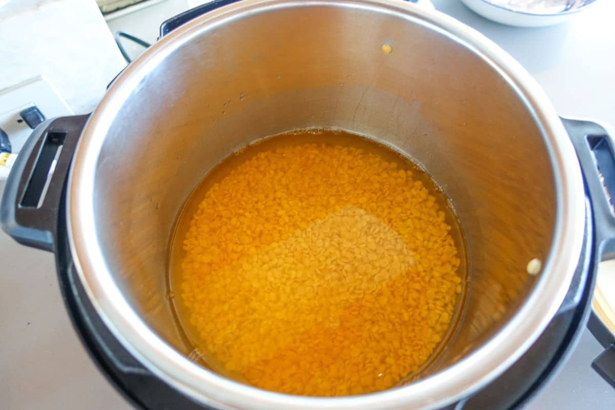 An instant pot contains yellow split lentils soaking in water along with salt and turmeric powder.