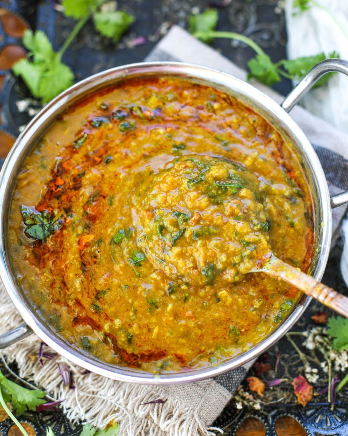 A pot of cooked spinach dal fry with cilantro and garlic tadka, and a ladle lifting a portion from the center.