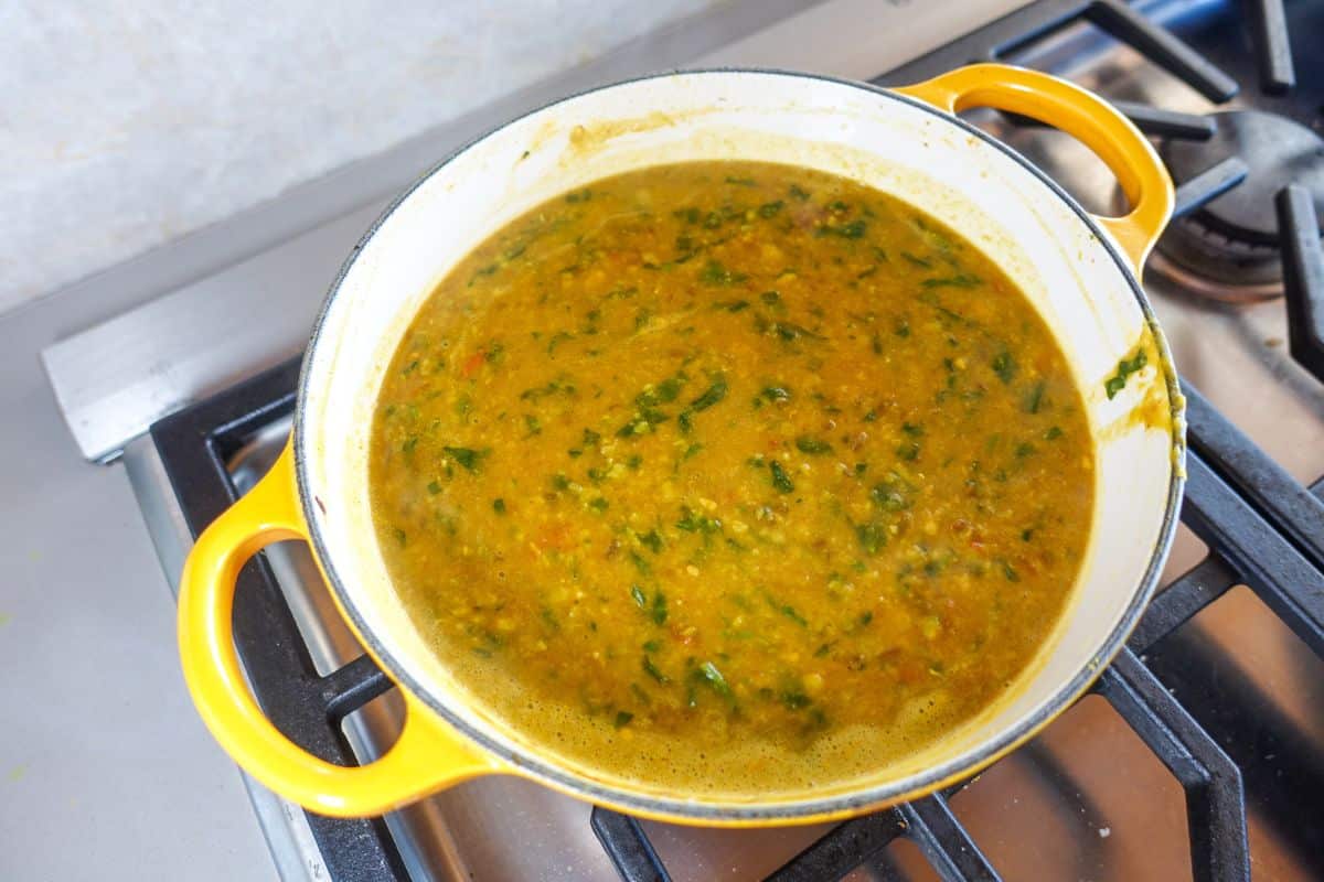 A yellow pot filled with a yellow spinach dal with visible herbs sits on a stove burner.