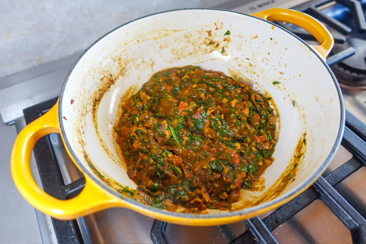 A yellow pot on a stovetop containing a cooked mixture of chopped greens, tomatoes, and spices.