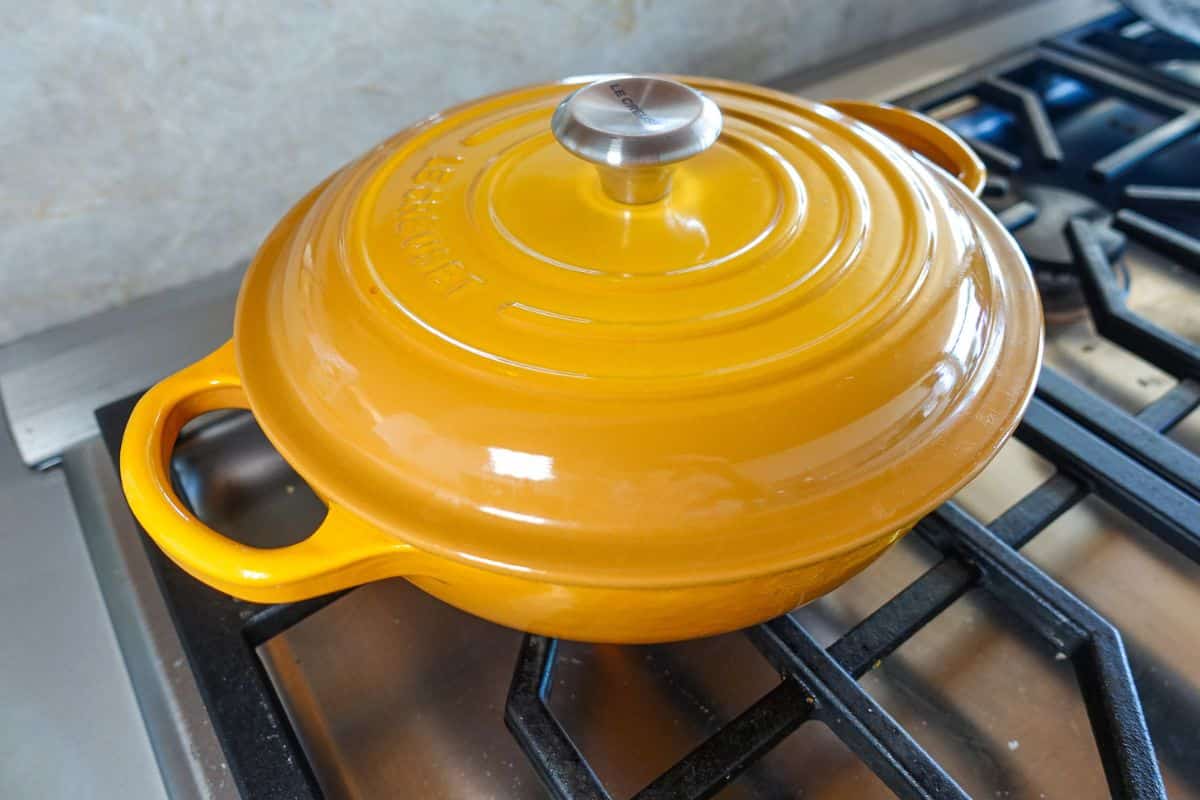 A yellow enameled cast iron Dutch oven with a lid sits on a gas stove burner.