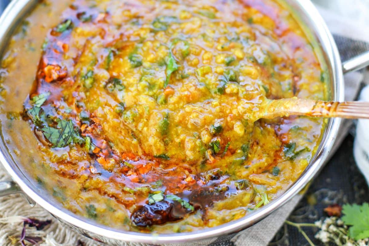 A close-up of a bowl of spinach dal fry, an Indian lentil curry garnished with chopped cilantro and a layer of spiced tadka oil on top, with a spoon partially submerged.