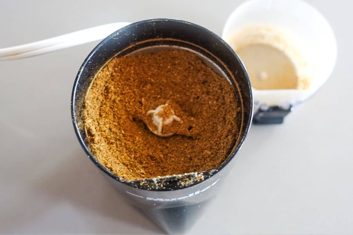 A top-down view of a coffee grinder filled with ground spices for kadai paneer.