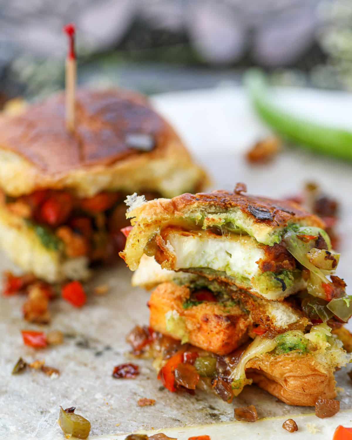 Paneer Tikka Sliders featuring a bite of the sandwich with a green chili in the background.