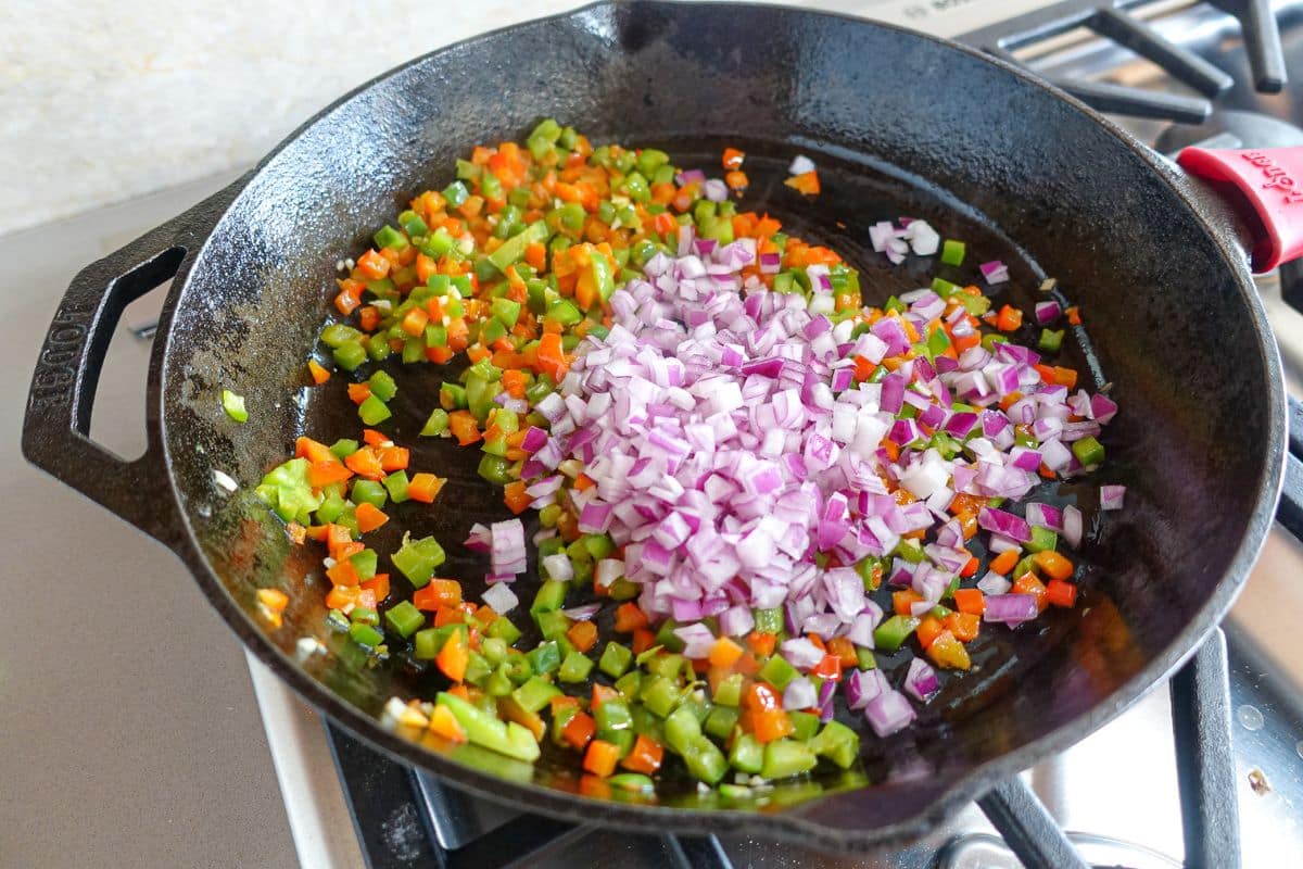 Add onions to the bell peppers in a castiron skillet.