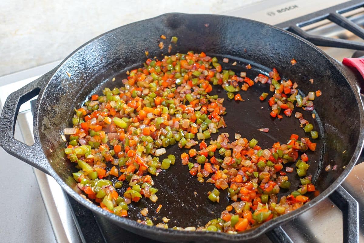 Bell peppers and onions are sauteed and browned in a cast-iron skillet.
