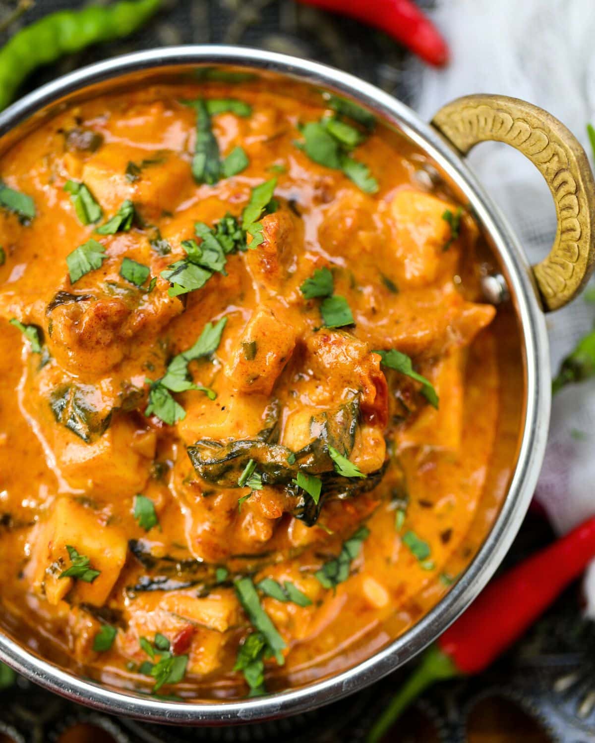 A copper bowl containing marry me paneer garnished with fresh cilantro with red & green chilies surrounding it.