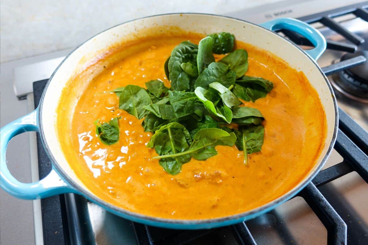 Add spinach leaves to a coconut milk sauce in an enameled braiser to make marry me paneer.