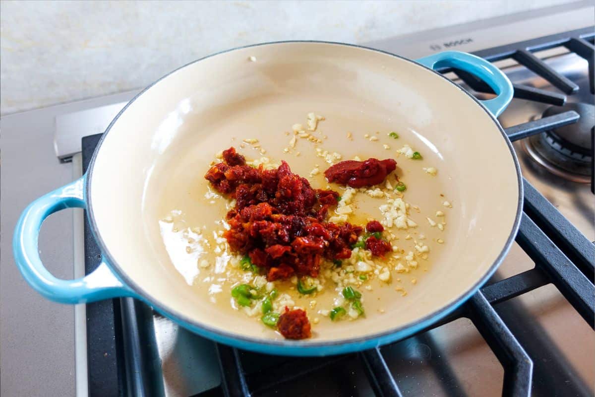 In a dutch oven, add oil, garlic, green chilies, sun-dried tomatoes, and tomato paste.