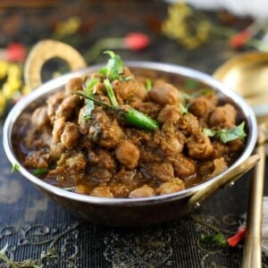 A copper bowl filled with Punjabi Chole garnished with cilantro and green chili, placed on a decorative dark tablecloth.
