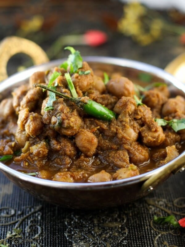 A copper bowl filled with Punjabi Chole garnished with cilantro and green chili, placed on a decorative dark tablecloth.