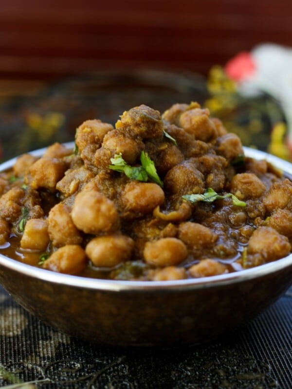 A bowl of Punjabi Chole garnished with fresh cilantro, placed on a dark ornate surface with colorful floral accents in the background.