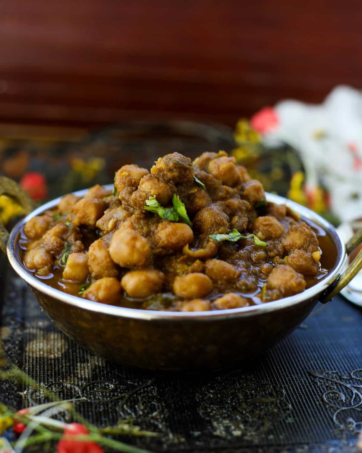 A bowl of Punjabi Chole garnished with fresh cilantro, placed on a dark ornate surface with colorful floral accents in the background.