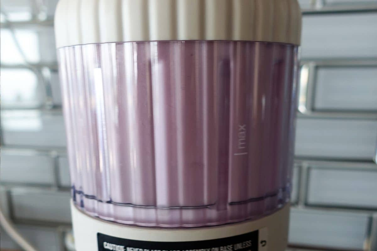 A close-up of a blender filled with blended purple onions, showing a max fill line, with a tiled backsplash in the background.