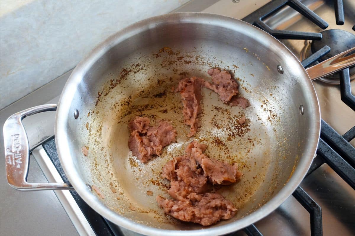 A stainless steel pan with cooked blended purple onions, showing browned residue on the pan, sits on a gas stove.