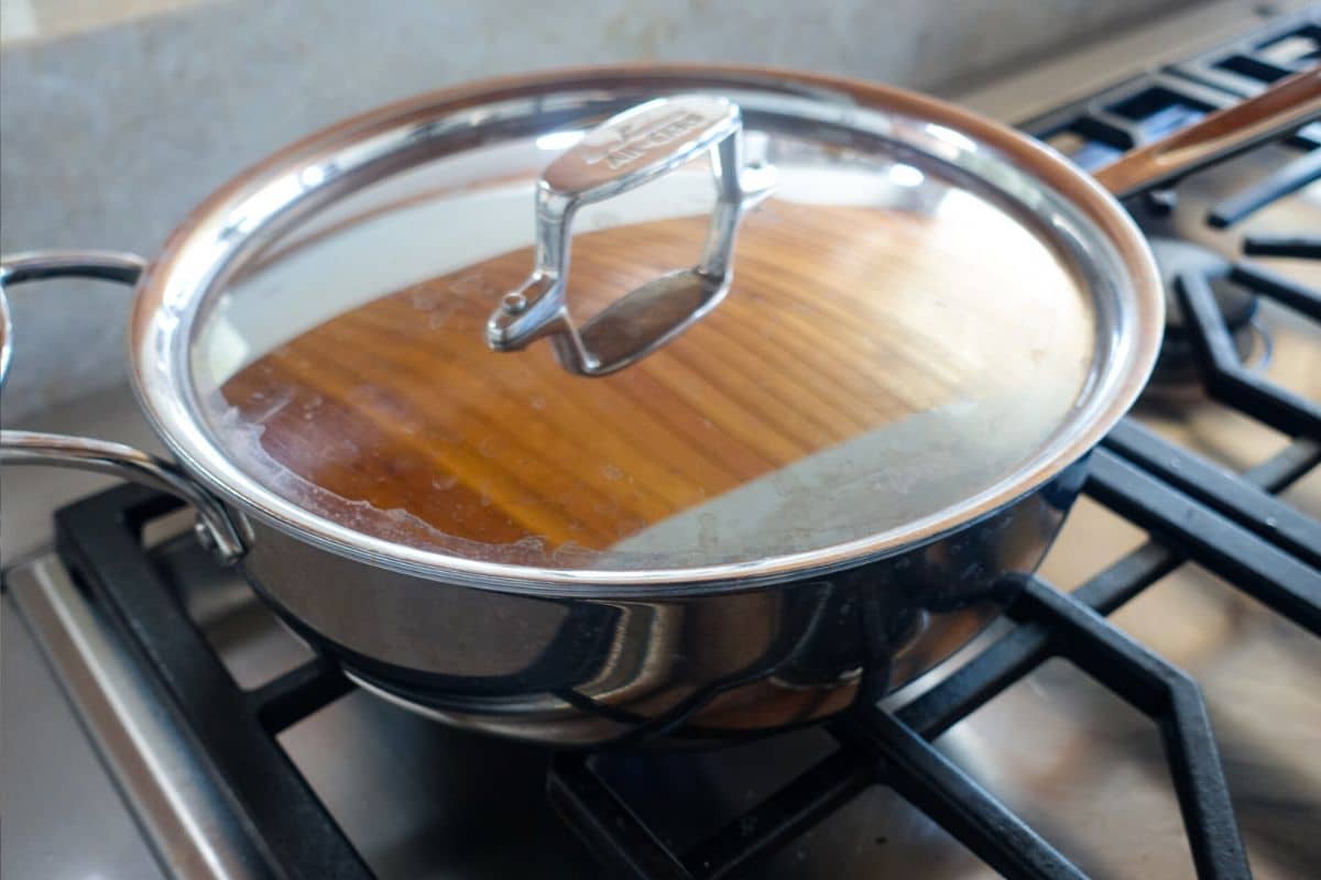 A stainless steel pan with a lid sits on a gas stove burner.