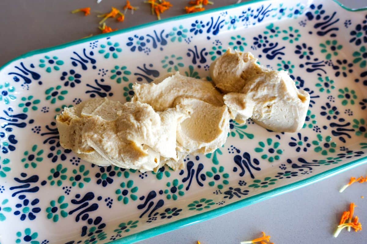 Three small scoops of hummus placed on a decorative rectangular plate with a blue and green floral pattern.