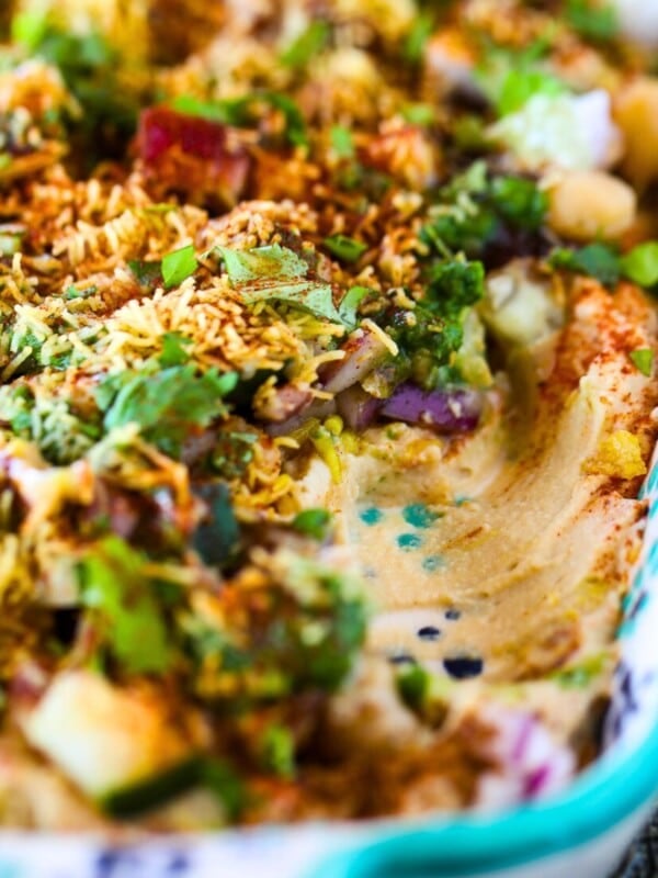 Close-up of Hummus Chaat Dip topped with chickpeas, chopped vegetables, herbs, spices, and sev in a rectangular serving tray.