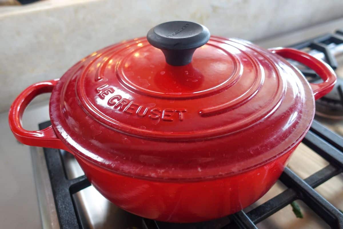 A red Le Creuset cast iron Dutch oven with lid on a stovetop burner.