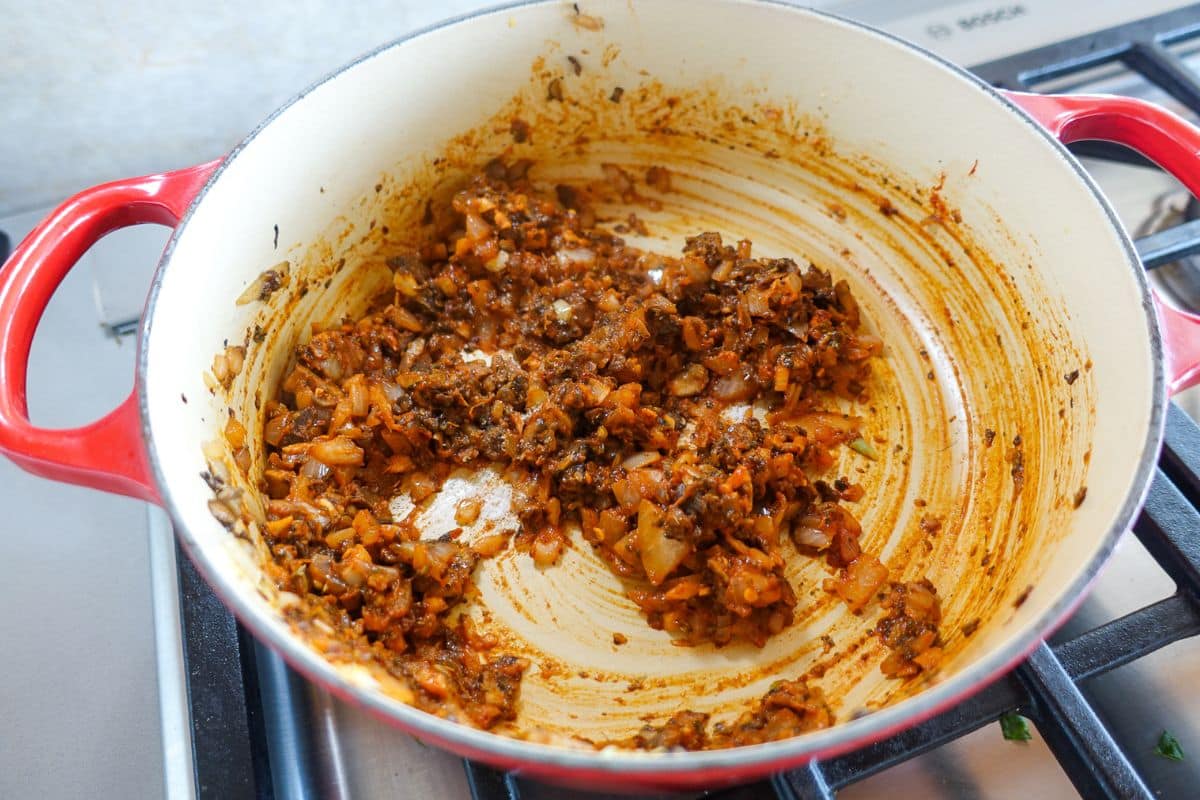 A red Dutch oven on a stove containing saut&eacute;ed chopped onions, mushrooms, garlic, and herbs.