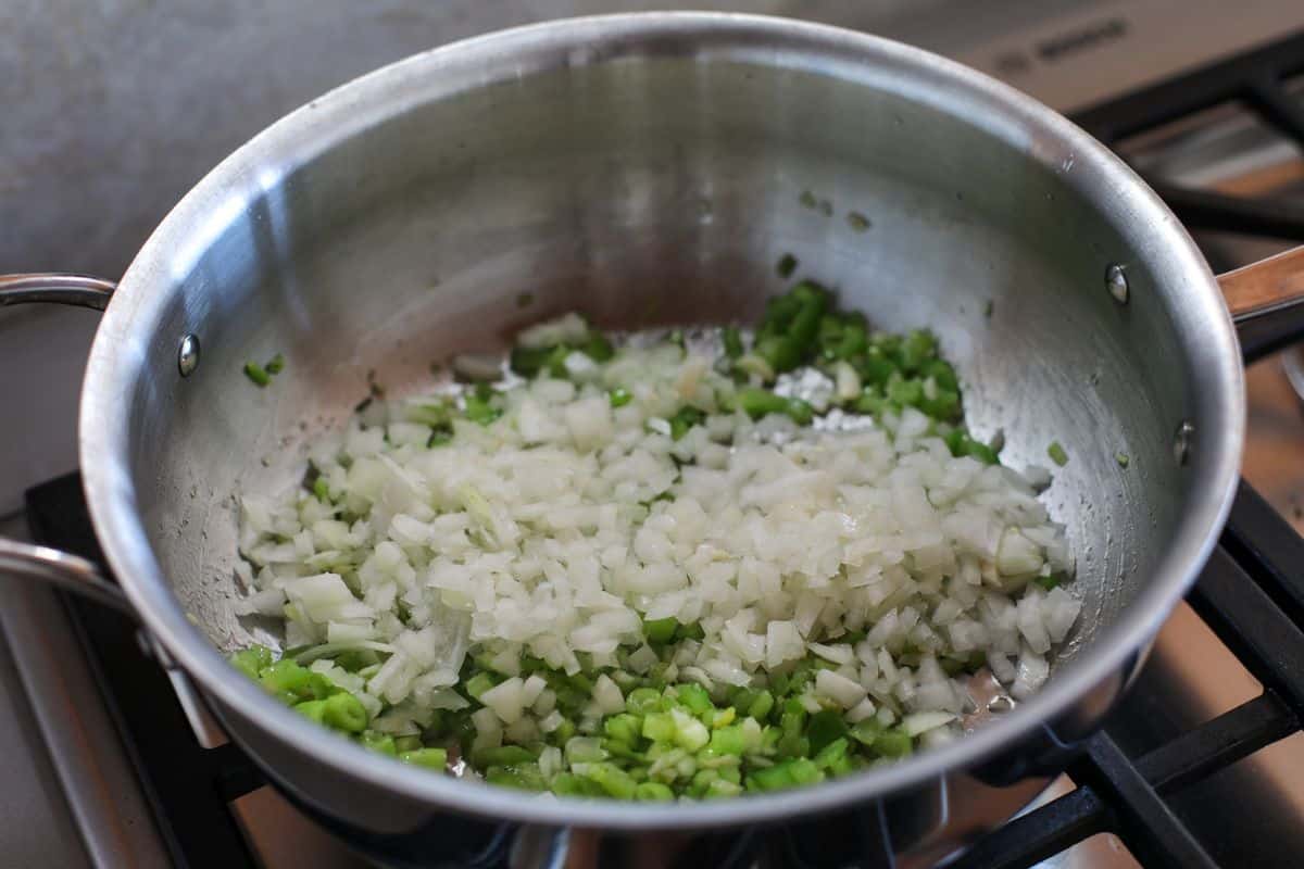 Chopped onions cooking in a stainless steel pan on a stove.