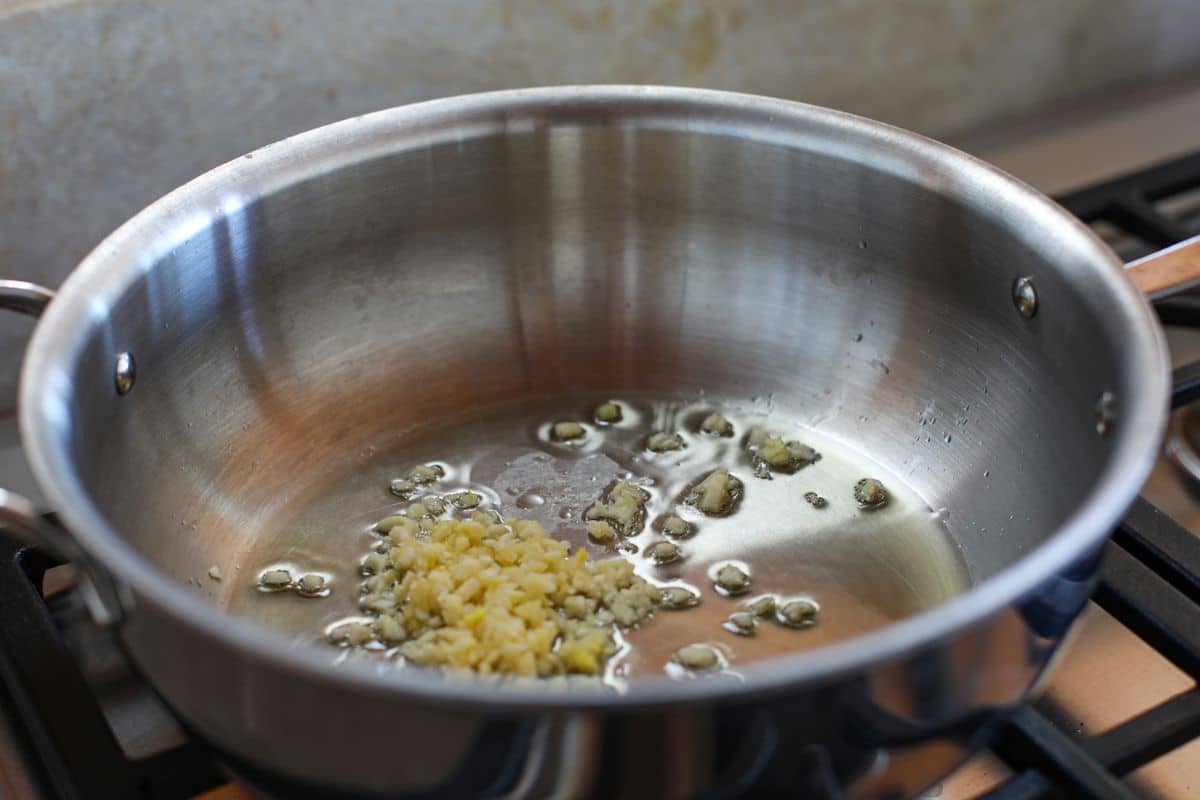 Minced garlic sautéing in oil in a stainless steel pan on a stovetop.