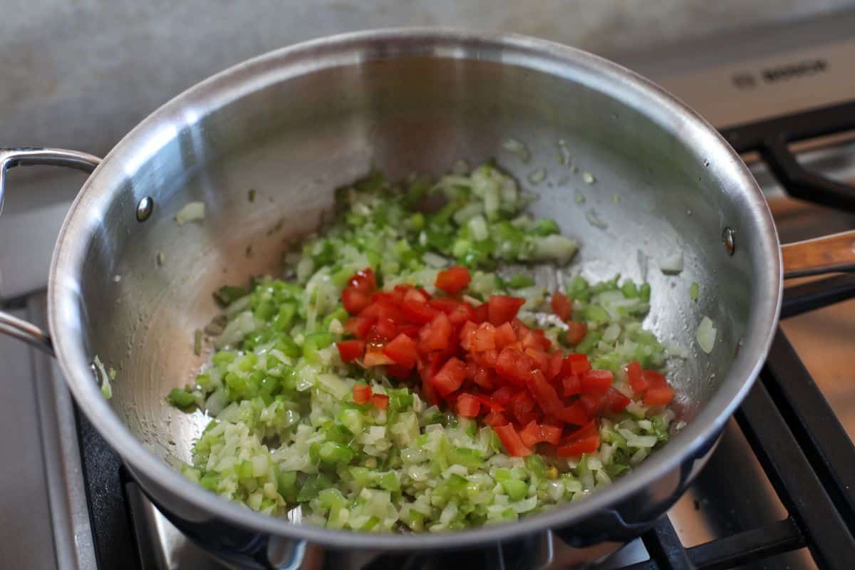 Tomatoes sautéing in a stainless steel pan on a stovetop.