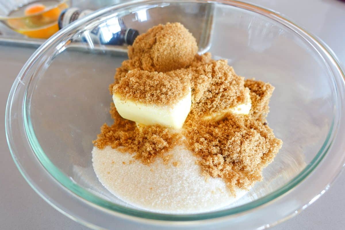 A glass bowl containing white sugar, light brown sugar, and butter.